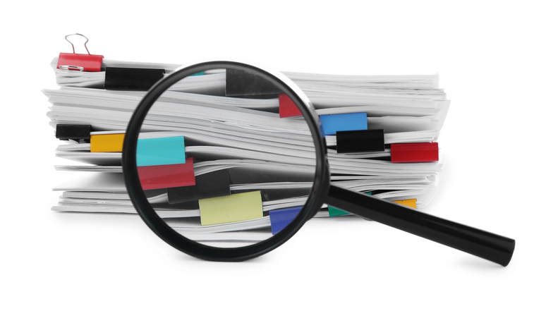 Stack of documents with binder clips and magnifying glass isolated on white